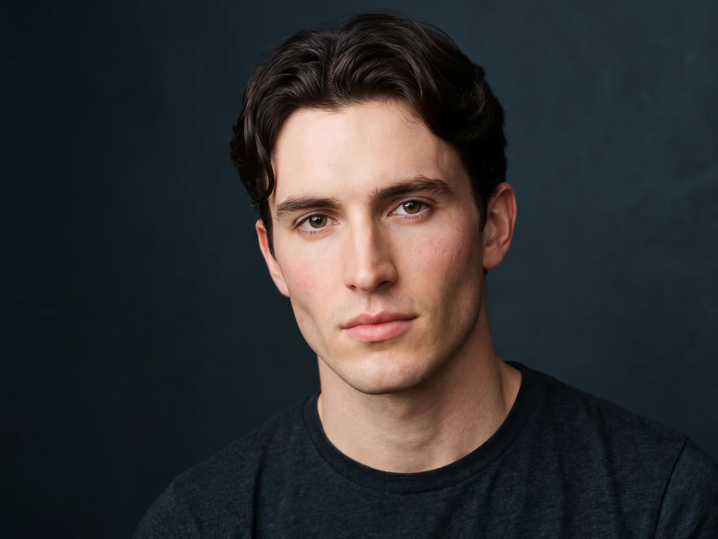 The same young man in a studio headshot on a graphite backdrop